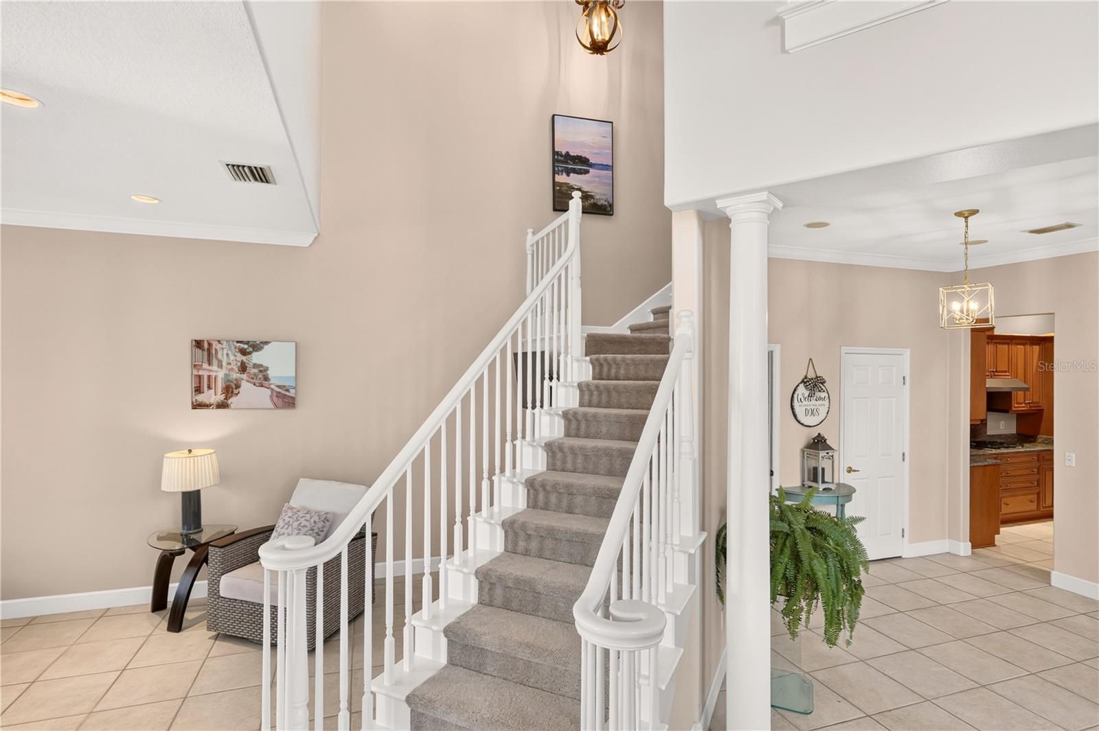Foyer with carpeted staircase, white railings, tiled floors, and a small sitting area.