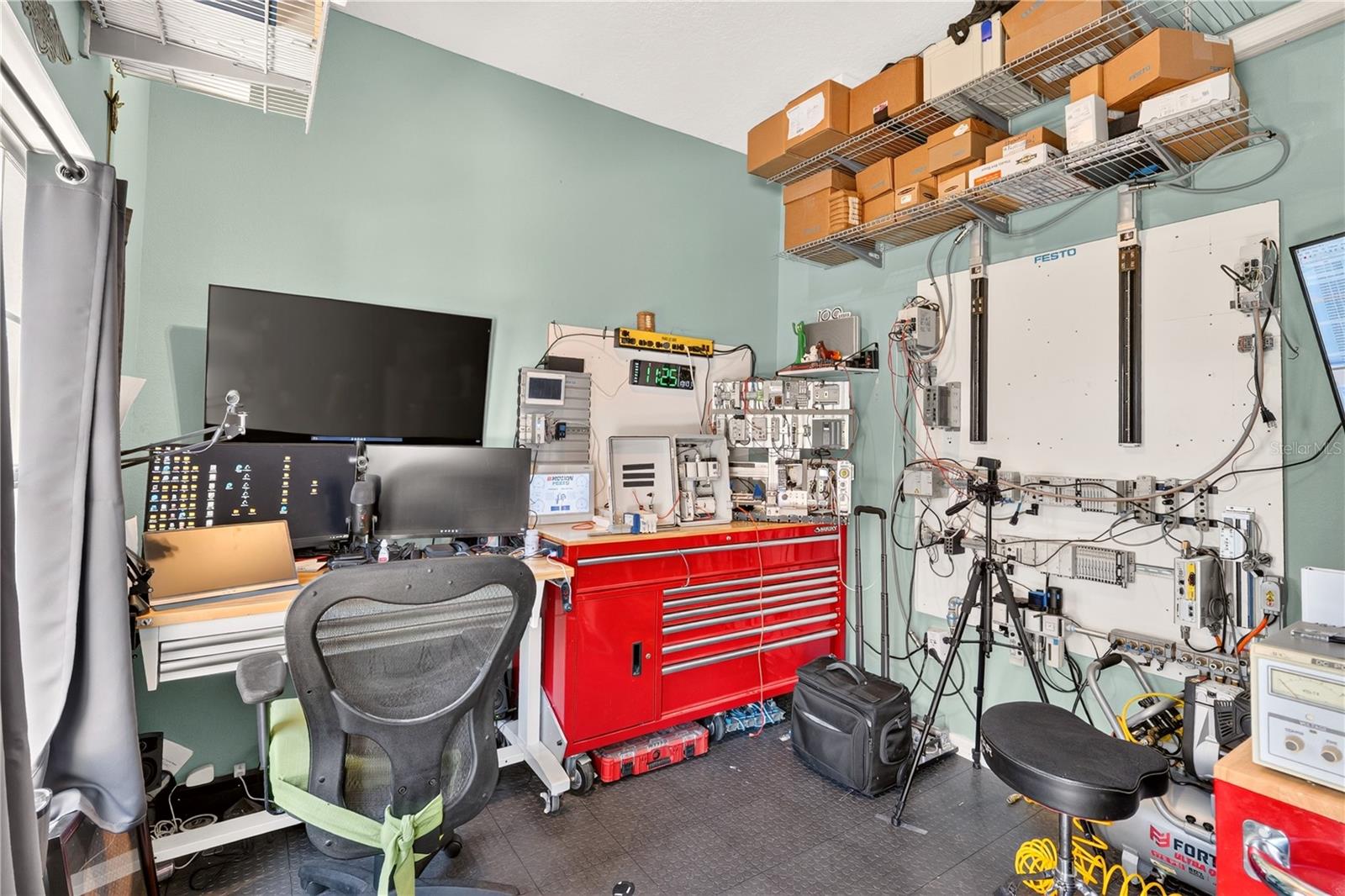 Electronics workshop with multiple monitors, a red tool cabinet, and equipment mounted on the walls.