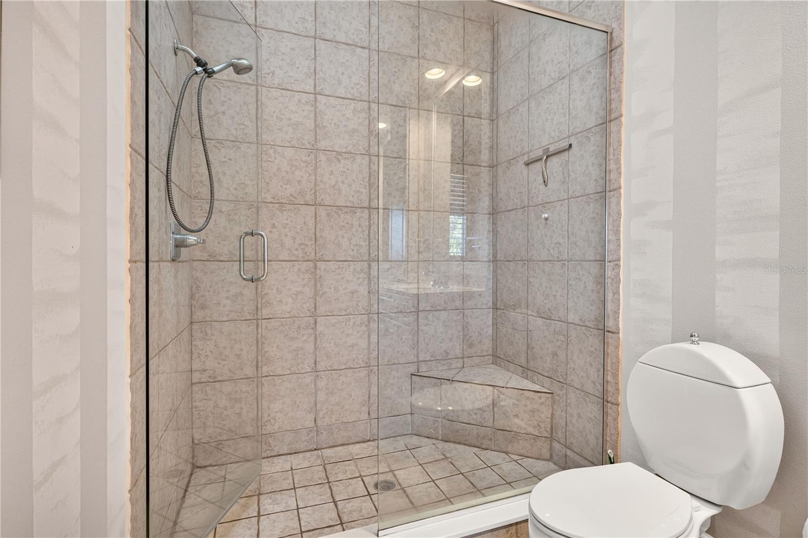 Tiled walk-in shower with clear glass enclosure and corner bench beside a white toilet.