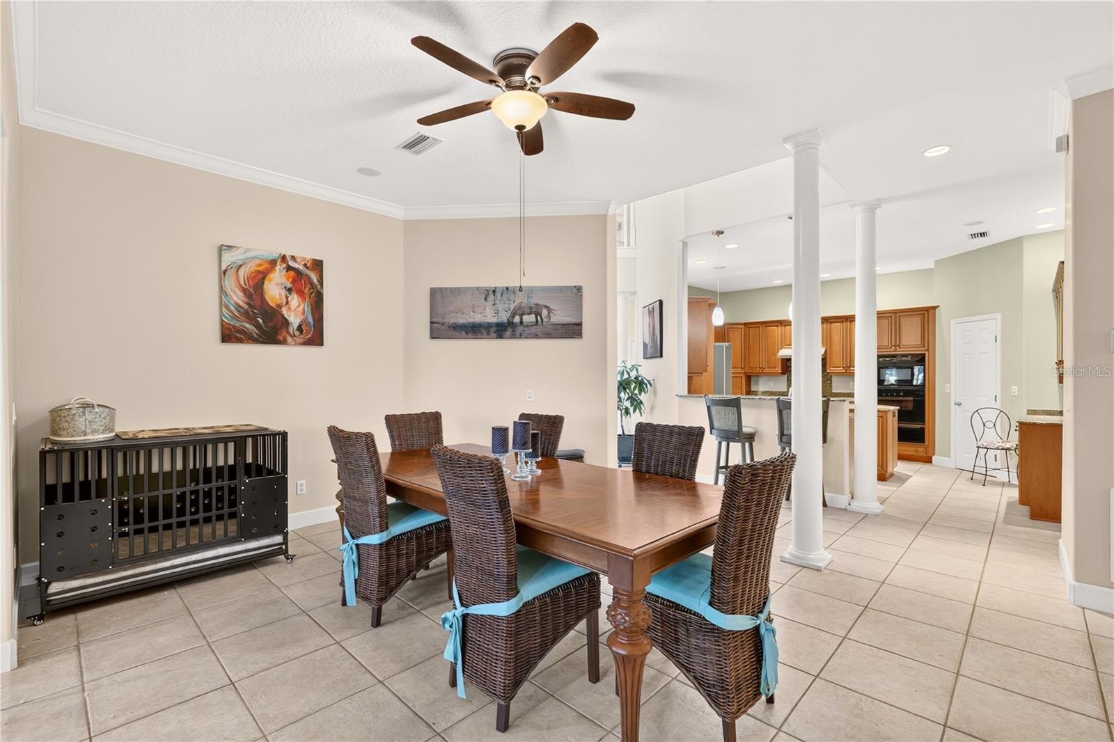Dining room with a wooden table and woven chairs opening onto a kitchen with wood cabinetry.