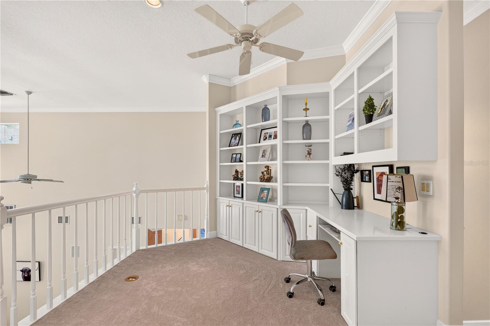 Upstairs home office with built-in white desk and shelving beside an open stairwell.