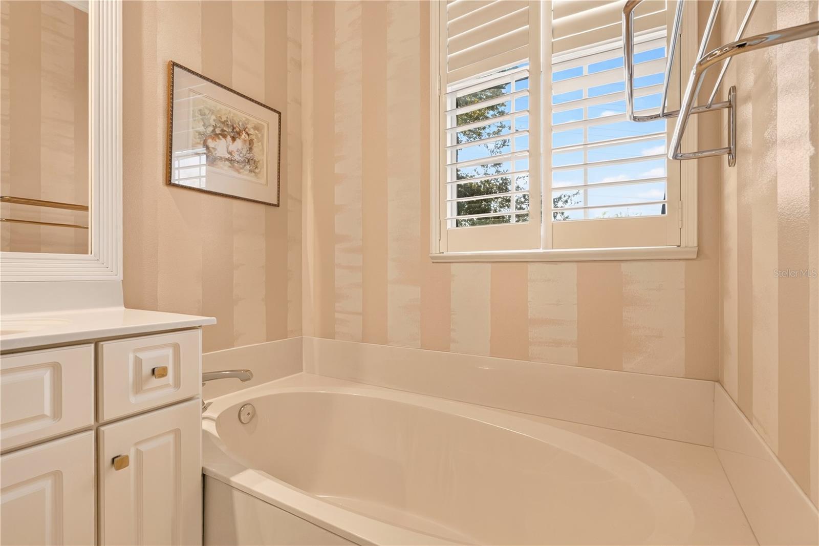 Bathroom with a built-in tub, white vanity, and plantation shutters.
