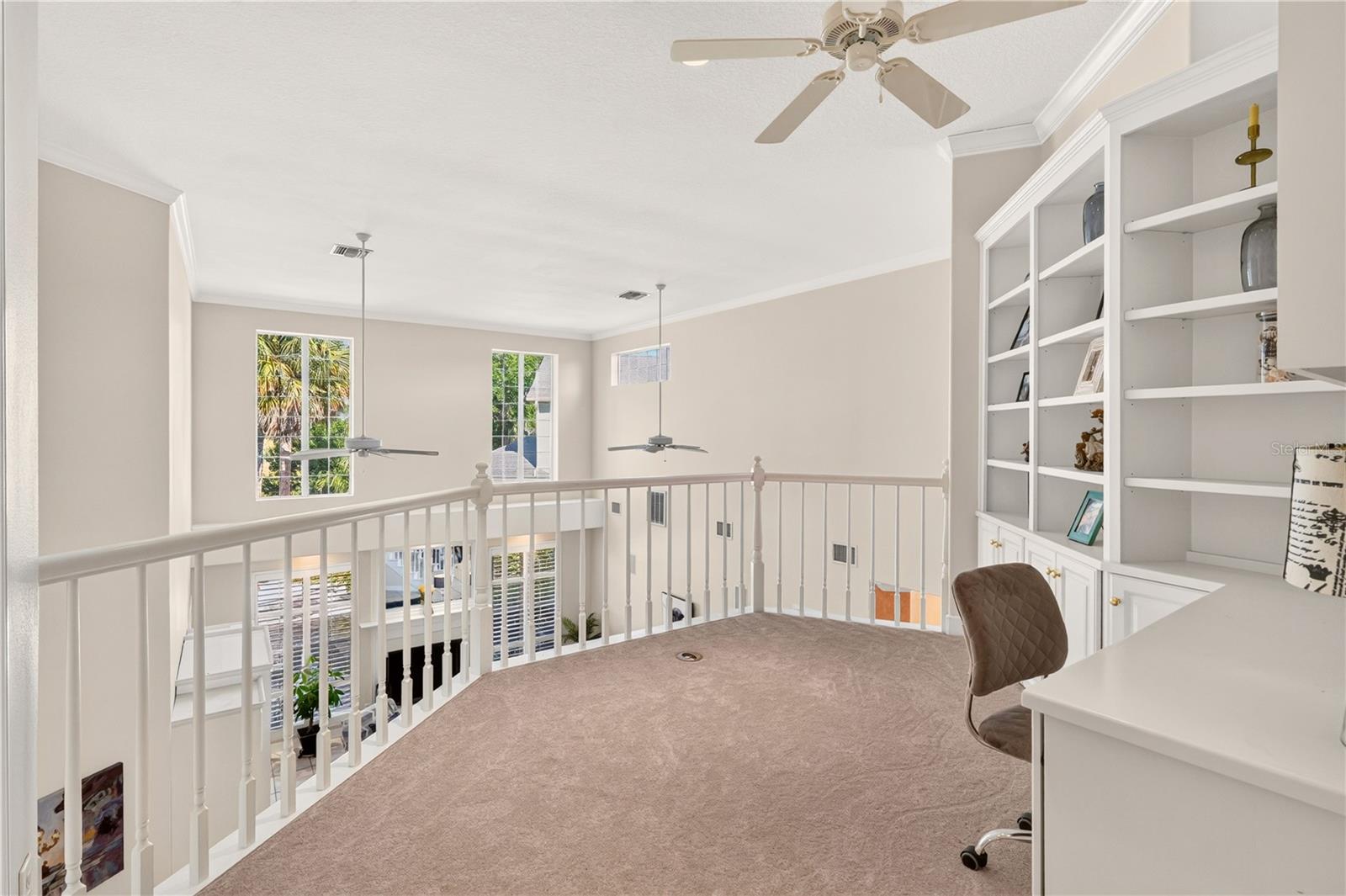 Upstairs loft office overlooking the foyer, with built-in shelving, a desk, ceiling fans, and carpet.