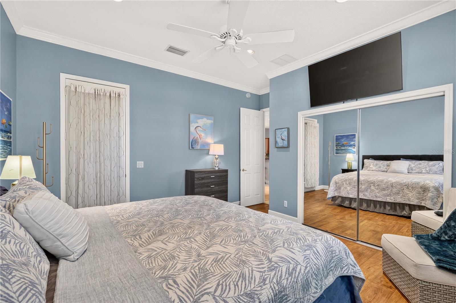 Furnished bedroom with blue walls, mirrored closet doors, and patterned bedding.