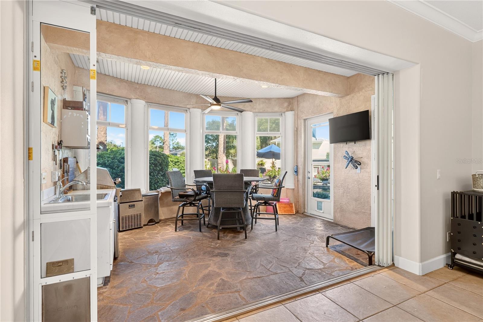 Enclosed sunroom with stone flooring, tall windows, and a dining table beneath a ceiling fan.