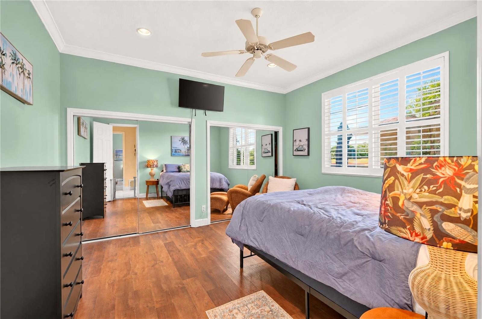 Bedroom with mint-green walls, wood flooring, shuttered windows, and mirrored closet doors.