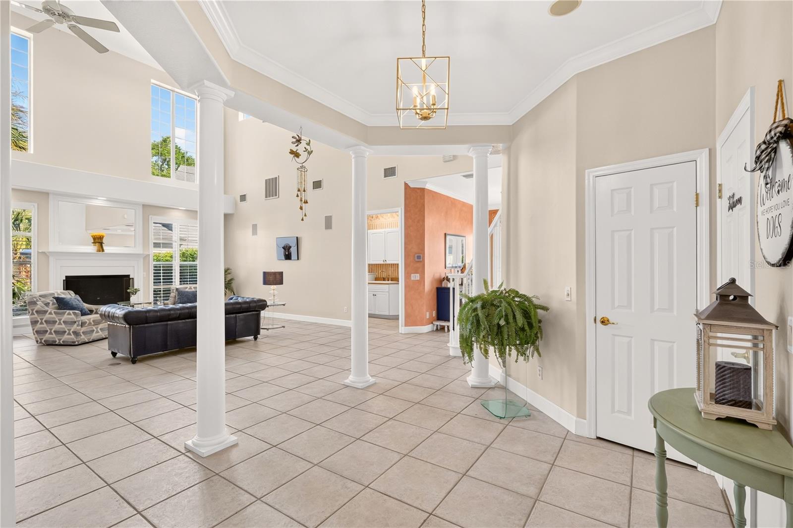 Foyer opening into a living room with white columns, high ceilings, tiled floors, and a fireplace.