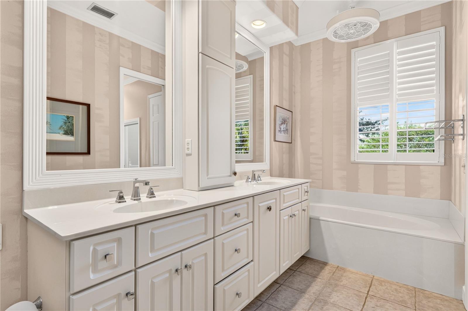 Bathroom with a long white vanity, large mirrors, bathtub, and plantation shutters.
