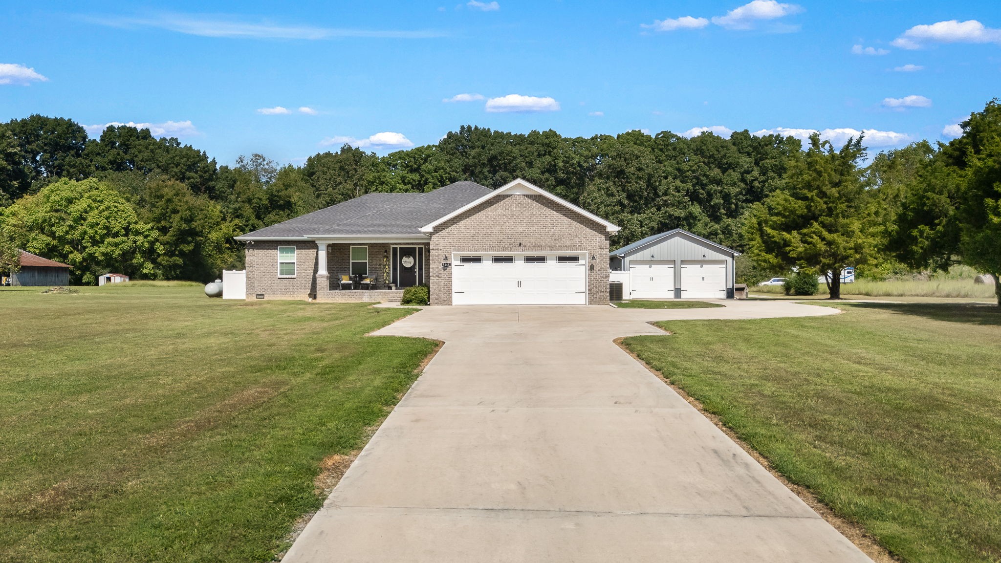 Brick single-story home with a wide driveway, detached garage, and expansive lawn.