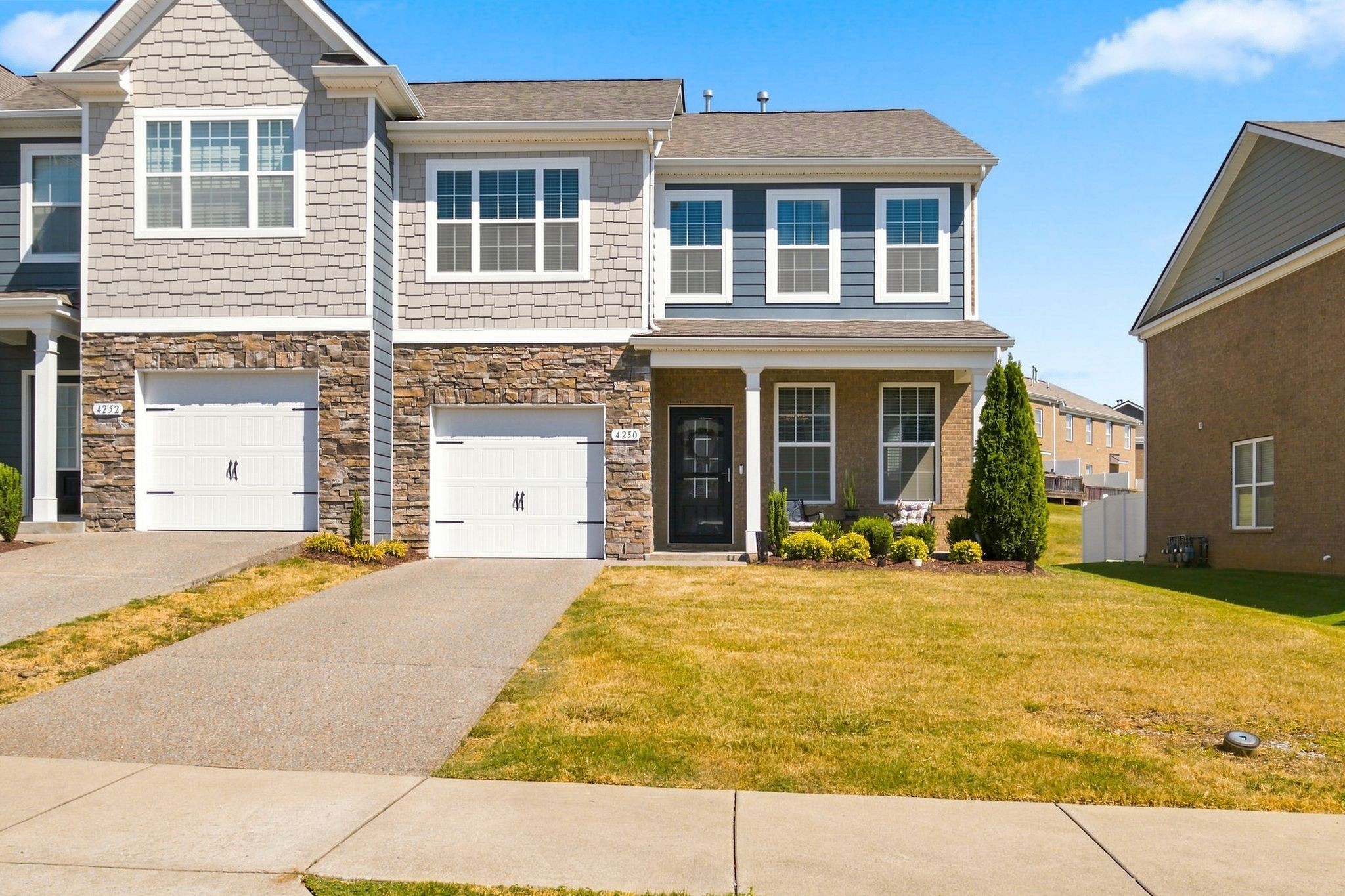 Two-story home with stone facade, gray shingle siding, white garage doors, and a covered front porch.