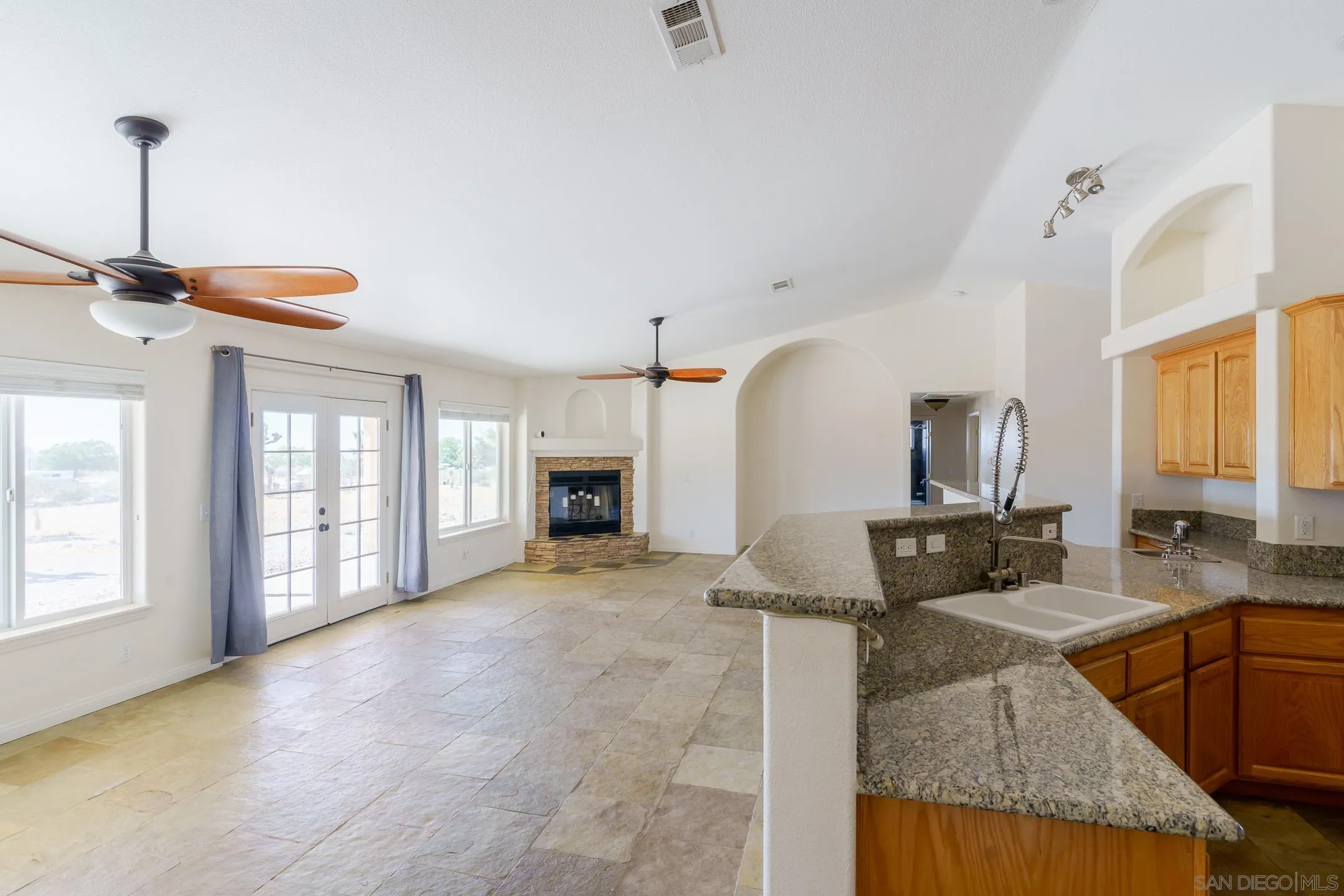 Open kitchen and living area with granite counters, tile floors, and a stone fireplace.