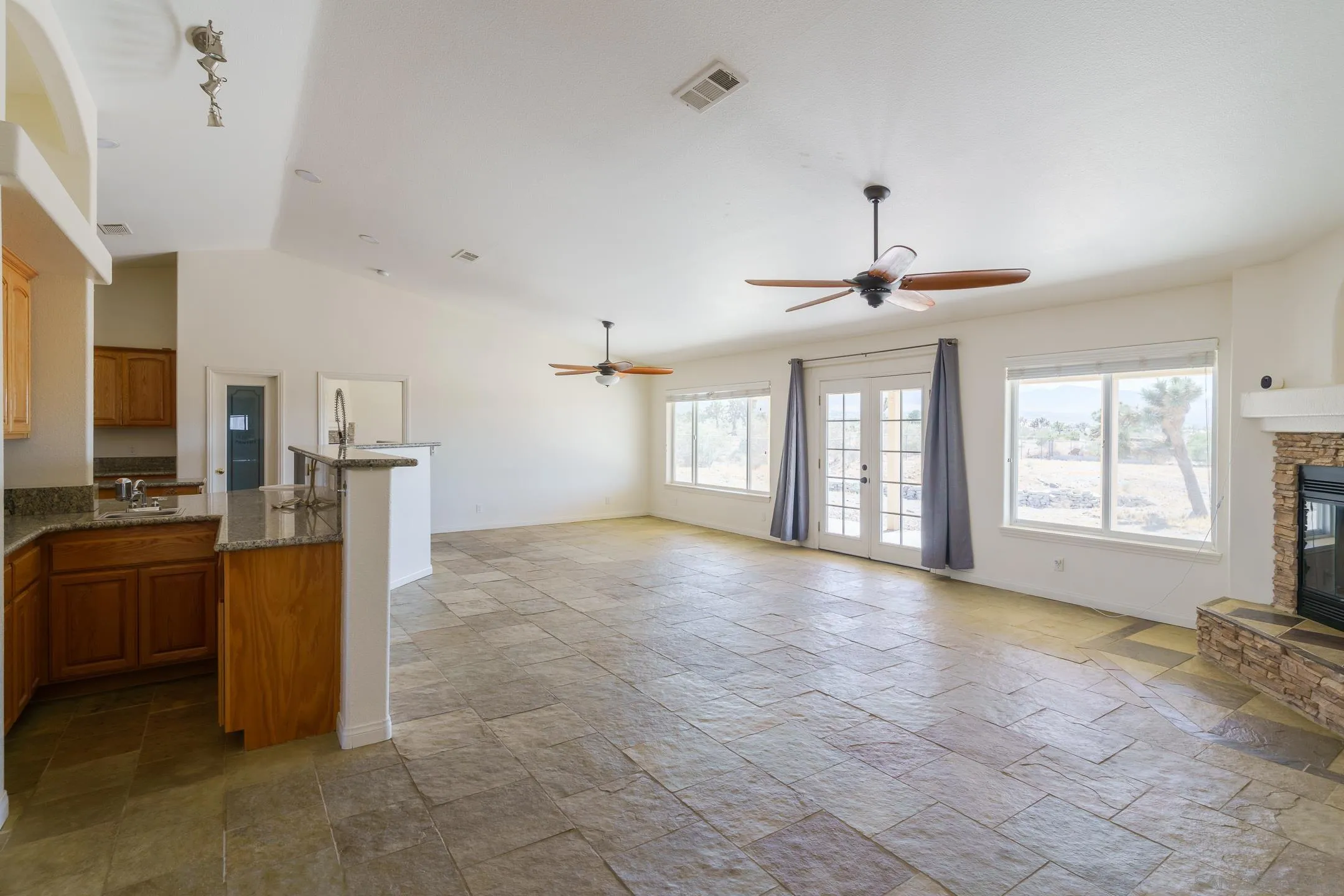 Open kitchen and living area with granite counters, tile floors, a stone fireplace, and French doors.
