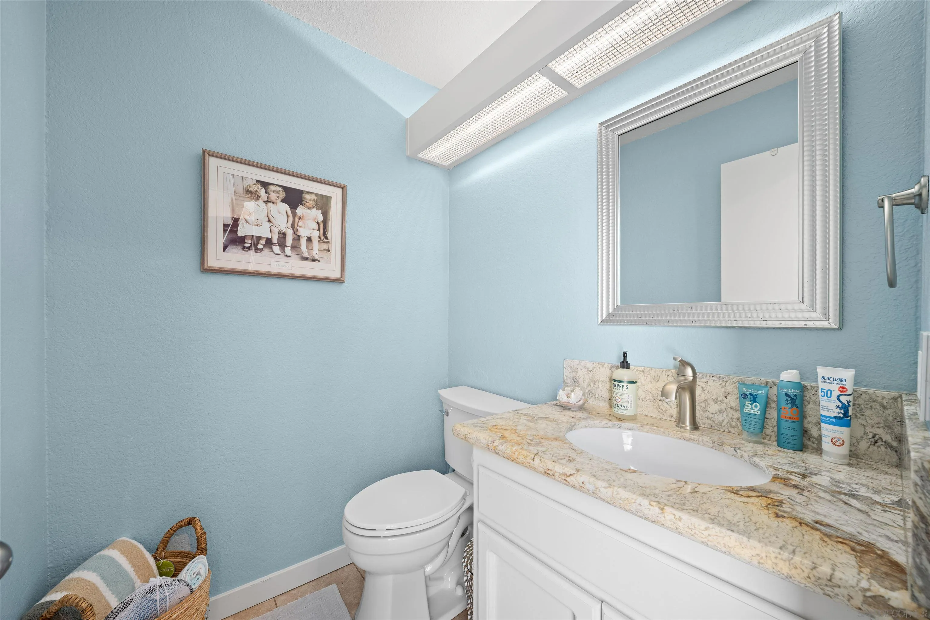 Bathroom with blue walls, a stone vanity countertop, white toilet, and large framed mirror.