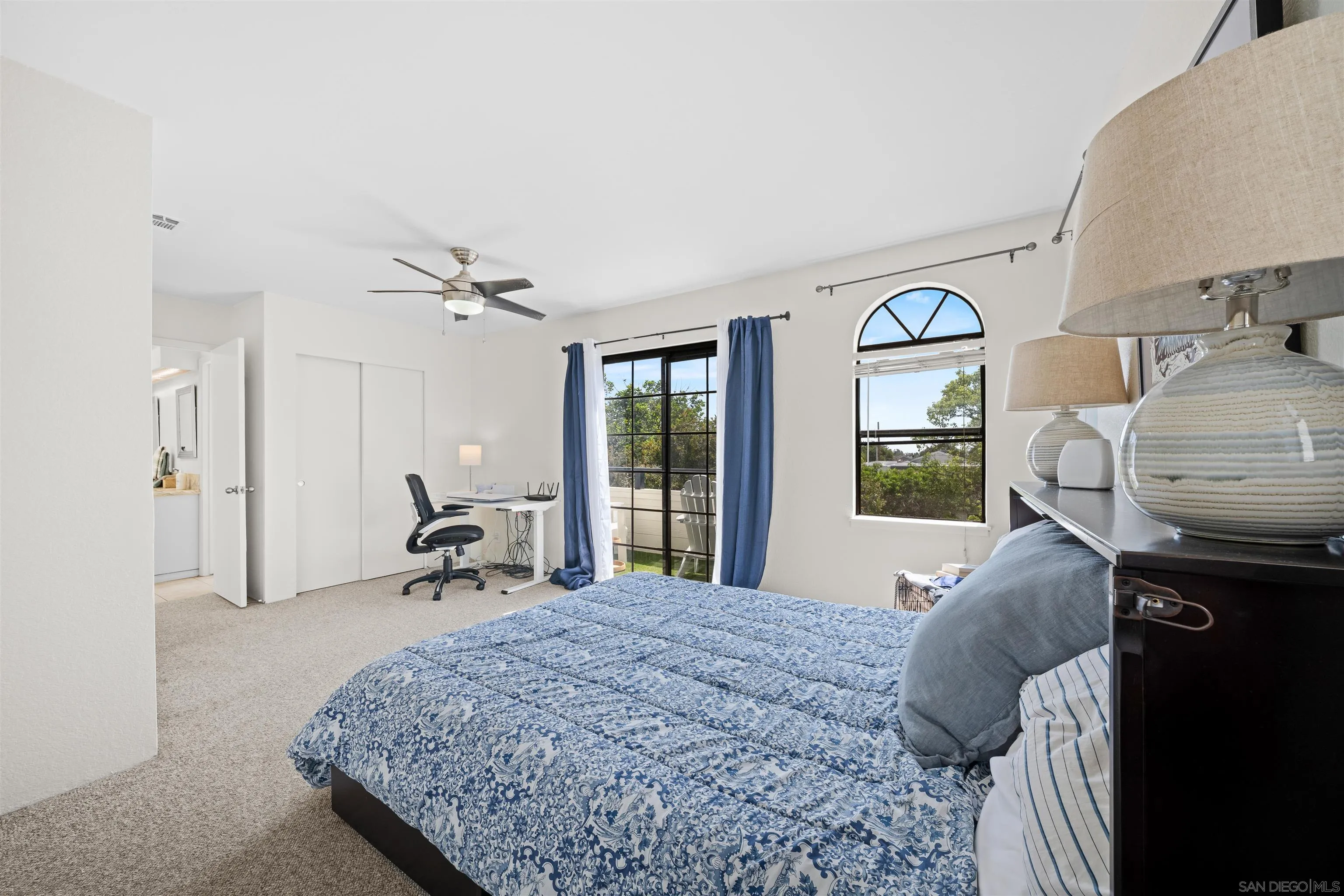 Bedroom with a blue patterned bed, desk, and arched window overlooking trees.