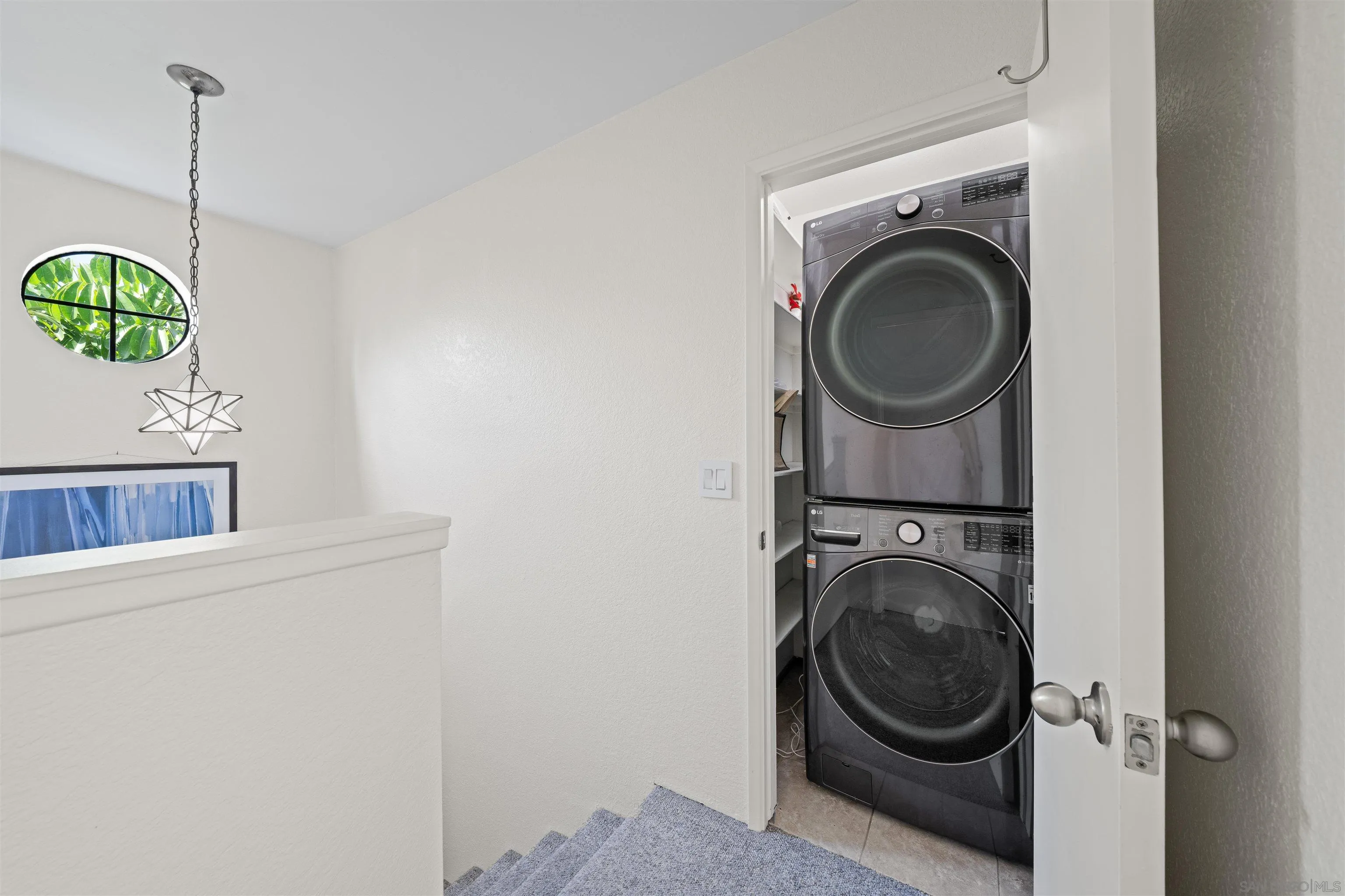 Stacked dark washer and dryer in a laundry closet beside a carpeted stair landing.