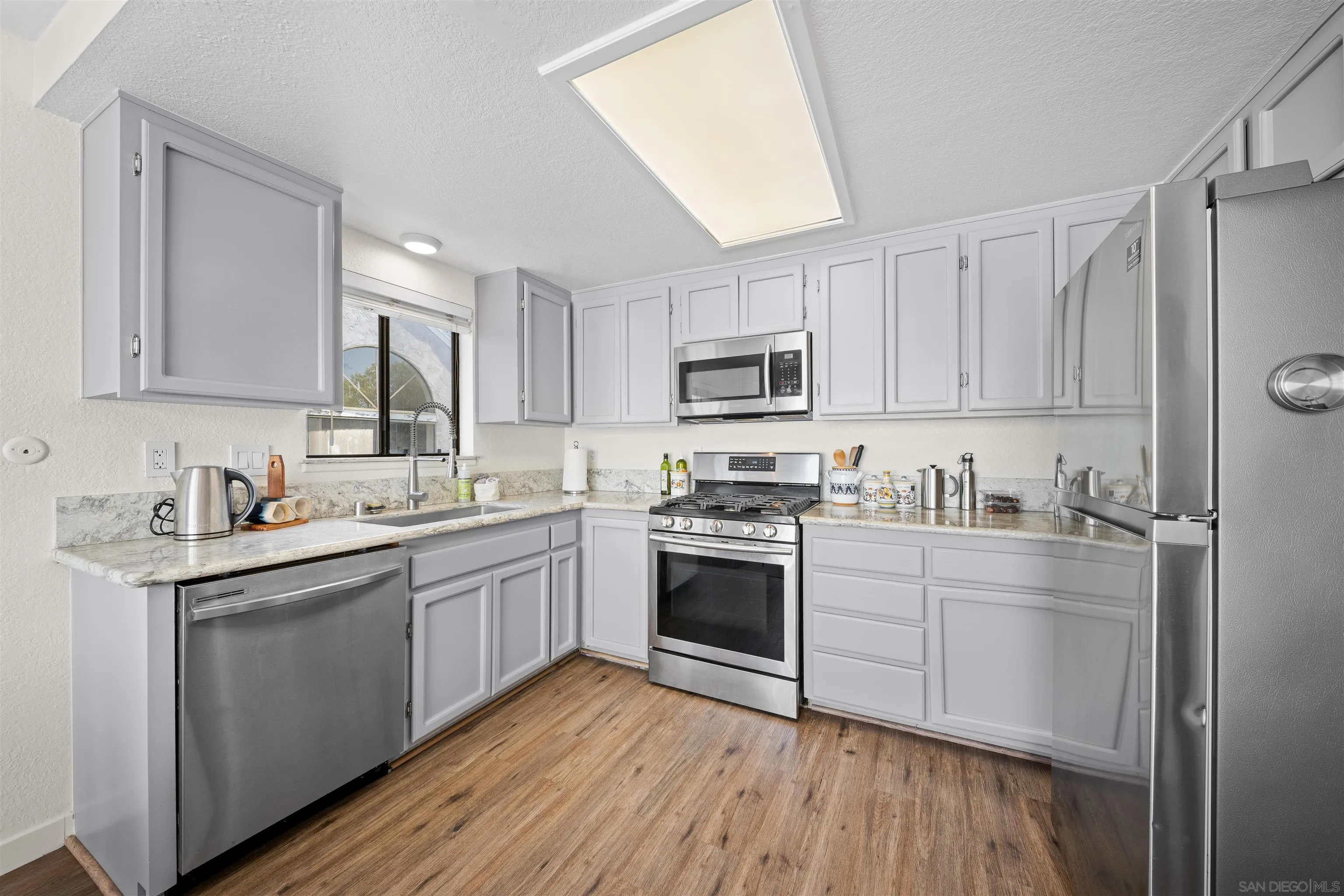 Kitchen with gray shaker cabinets, stone counters, stainless steel appliances, and wood-look flooring.