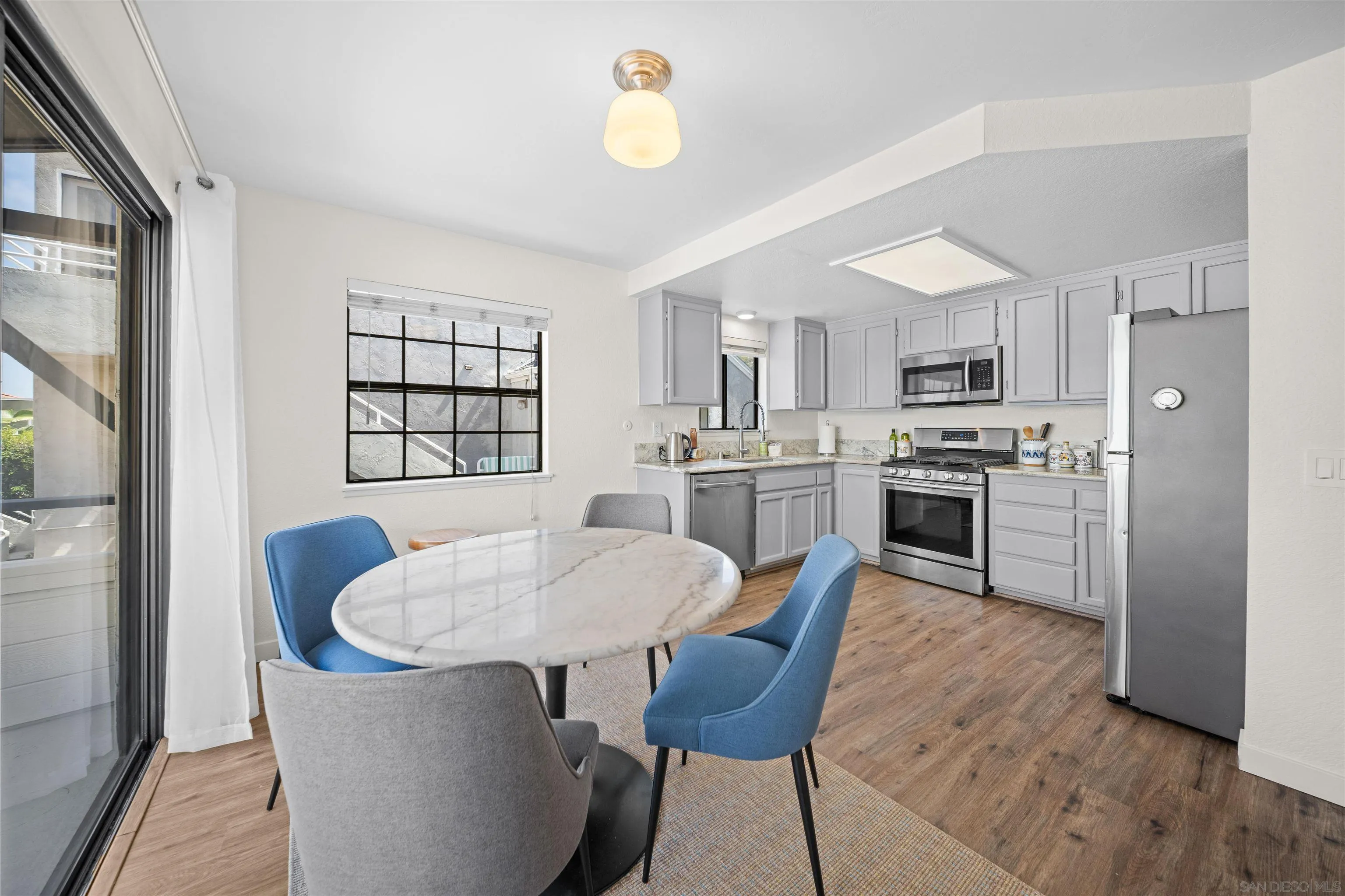 Kitchen and dining area with gray cabinetry, stainless appliances, and a marble-look table with blue chairs.