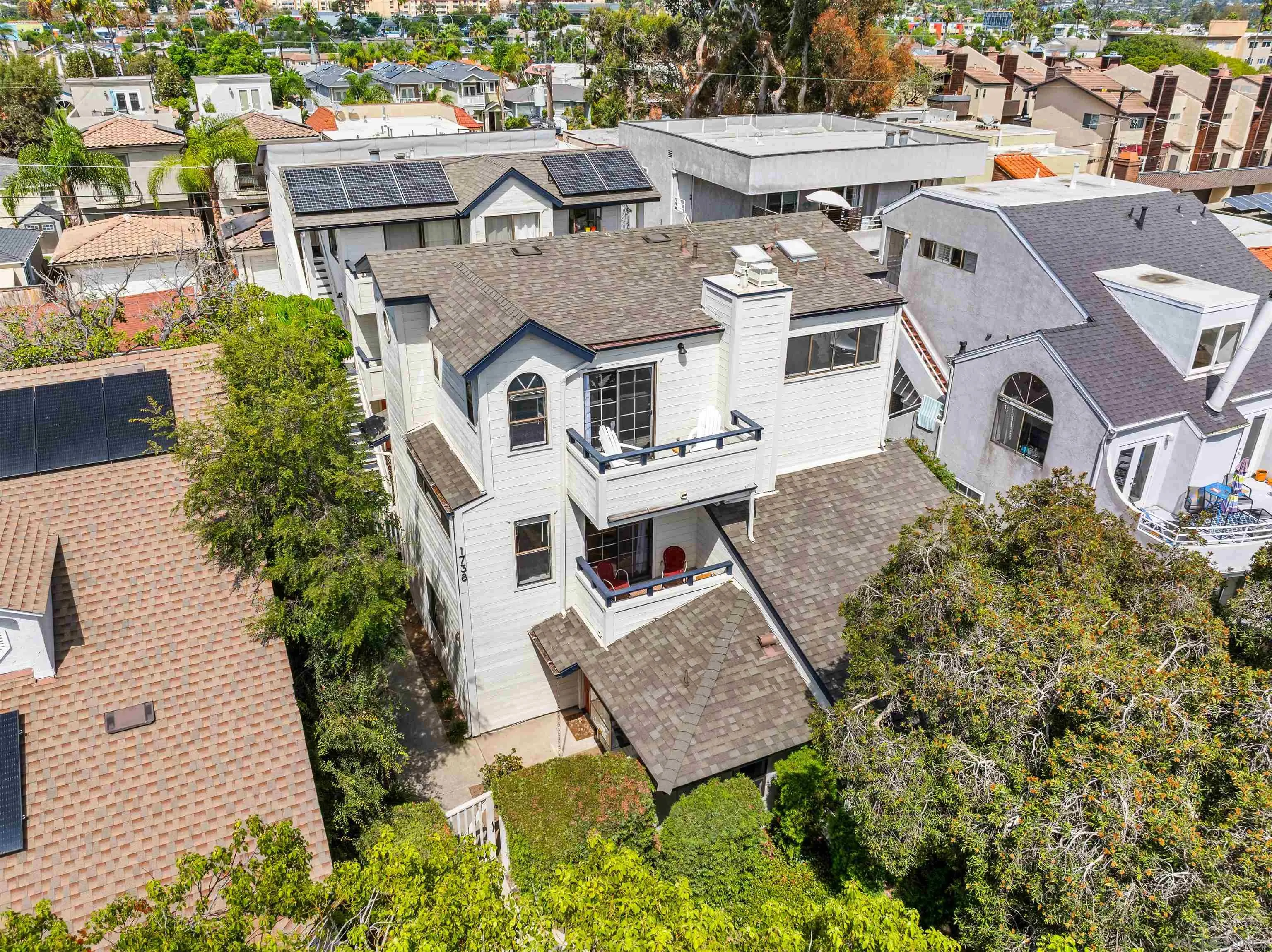 Aerial view of a white multi-story home with two balconies amid a dense residential neighborhood.