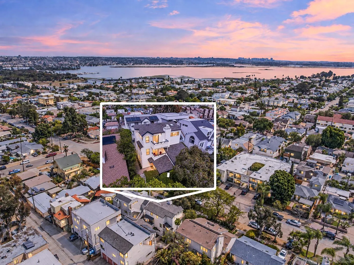 Aerial view of a home in a coastal neighborhood, with the bay glowing at dusk.