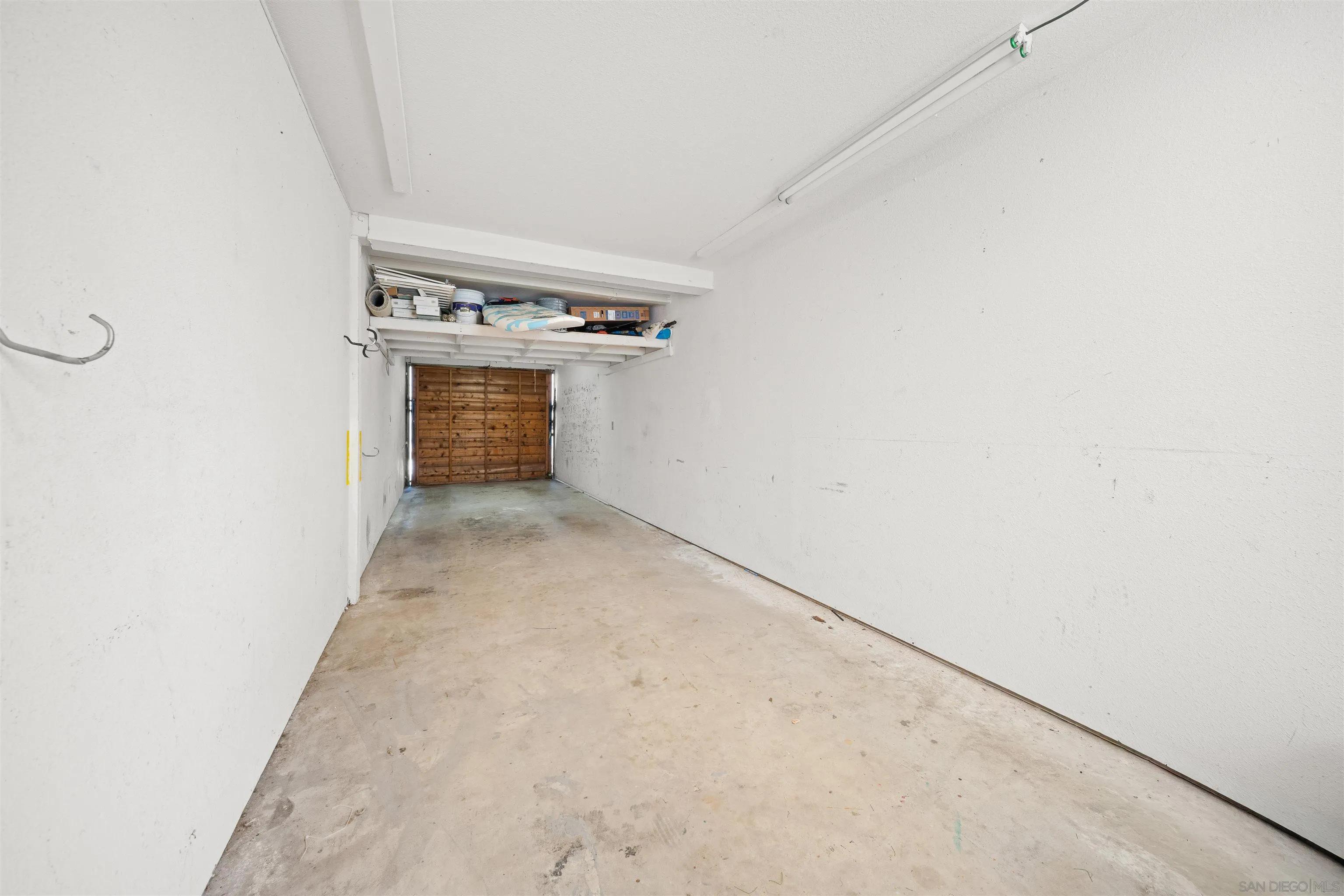 Long single-car garage with overhead storage shelves and a wooden door at the far end.