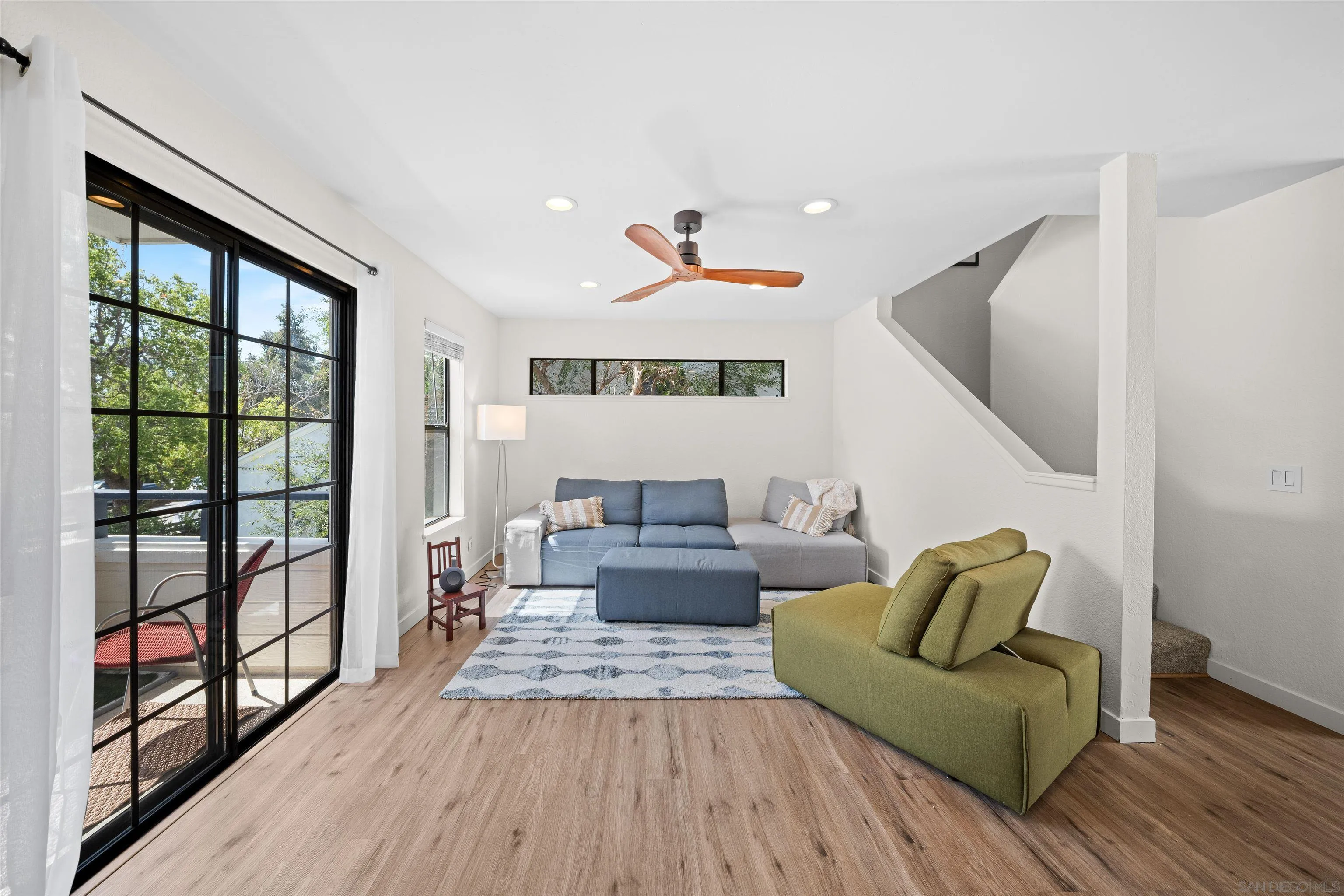 Furnished living room with a gray sectional, green chaise, and black-framed sliding doors to a balcony.