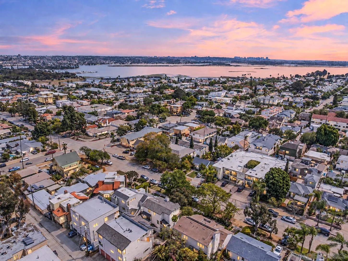Aerial view of a coastal neighborhood and bay beneath a pink sunset sky.