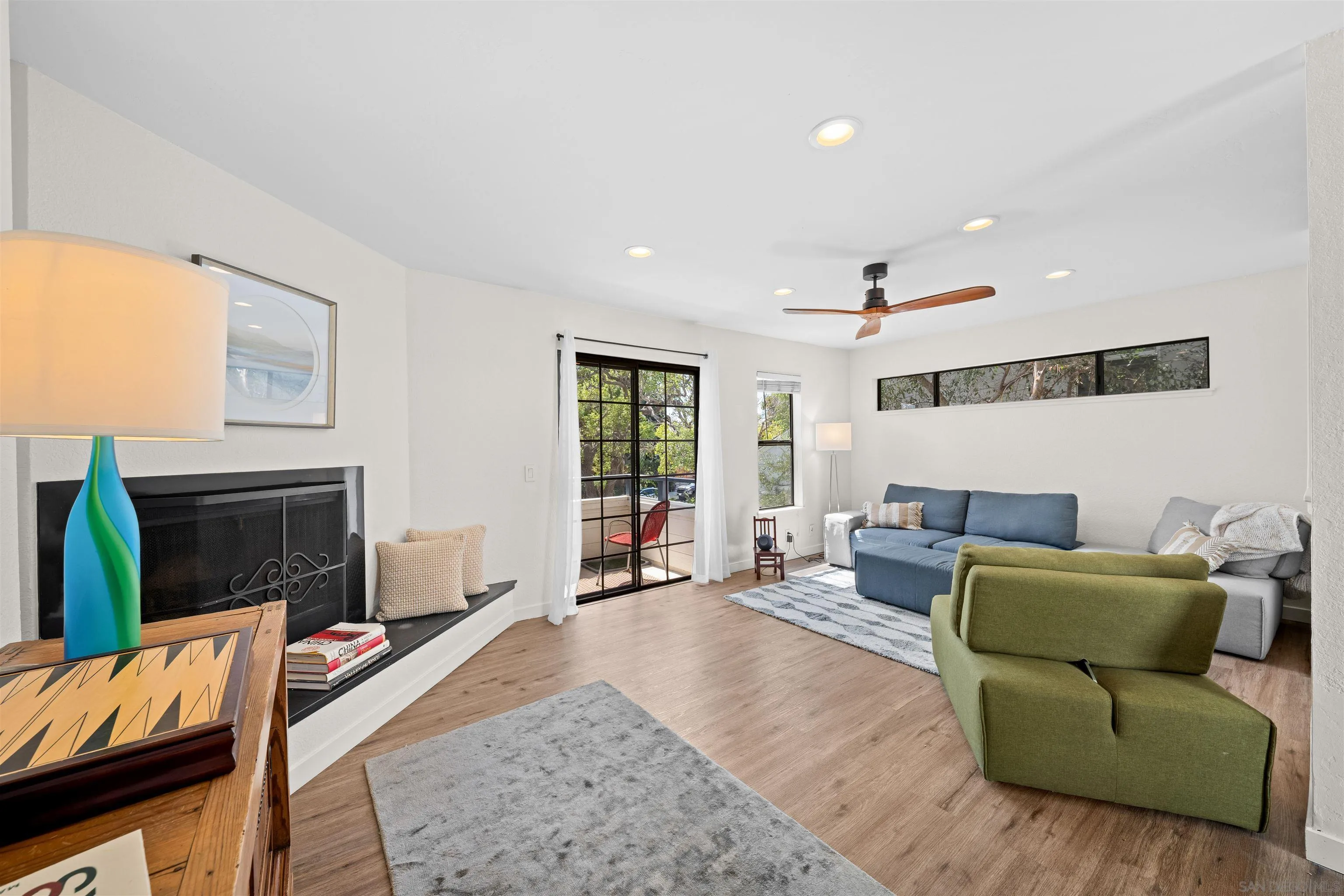 Living room with a fireplace, colorful seating, wood-look floors, and glass doors opening to a patio.