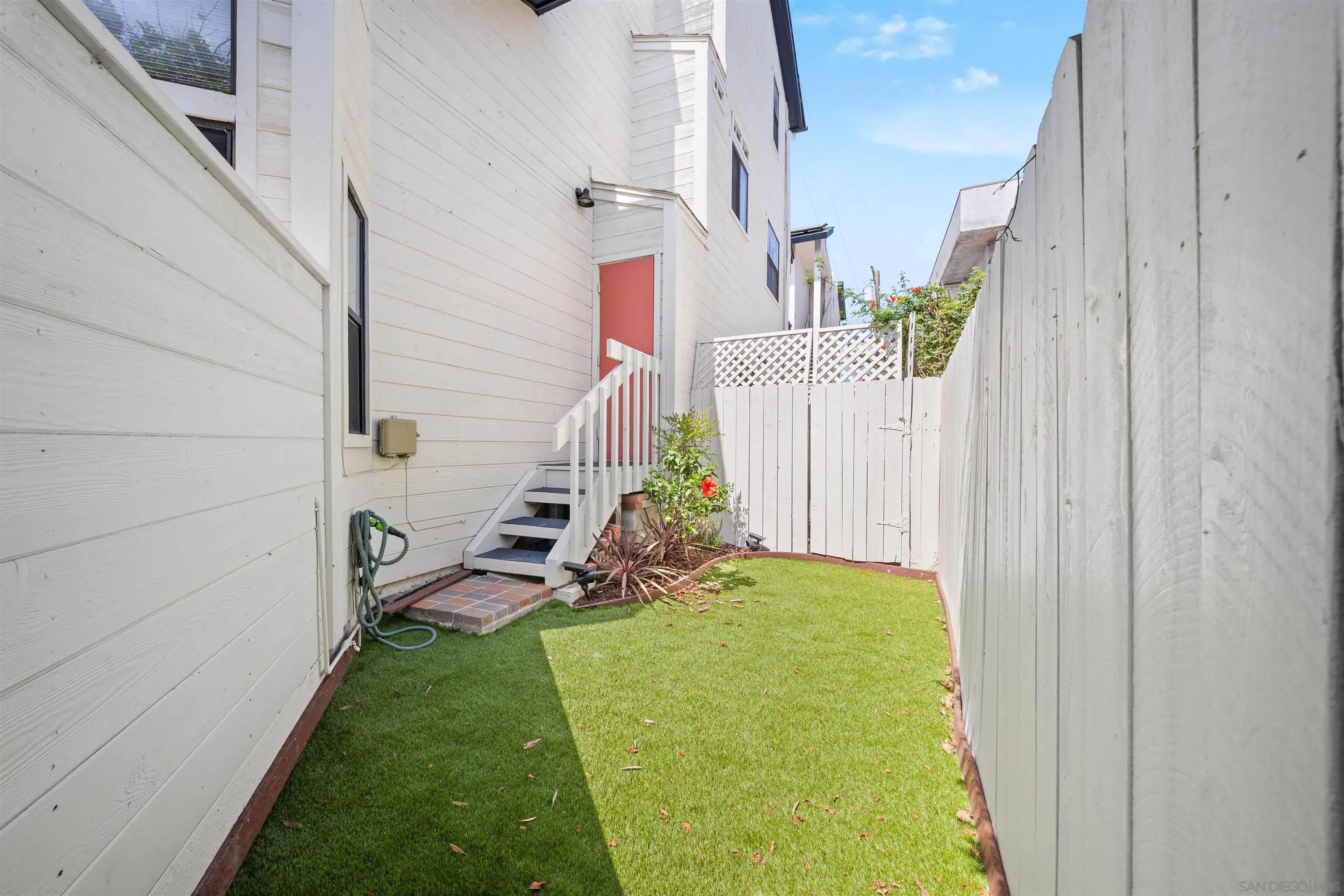 Fenced backyard with green lawn, a staircase to a red door, and small planted beds.