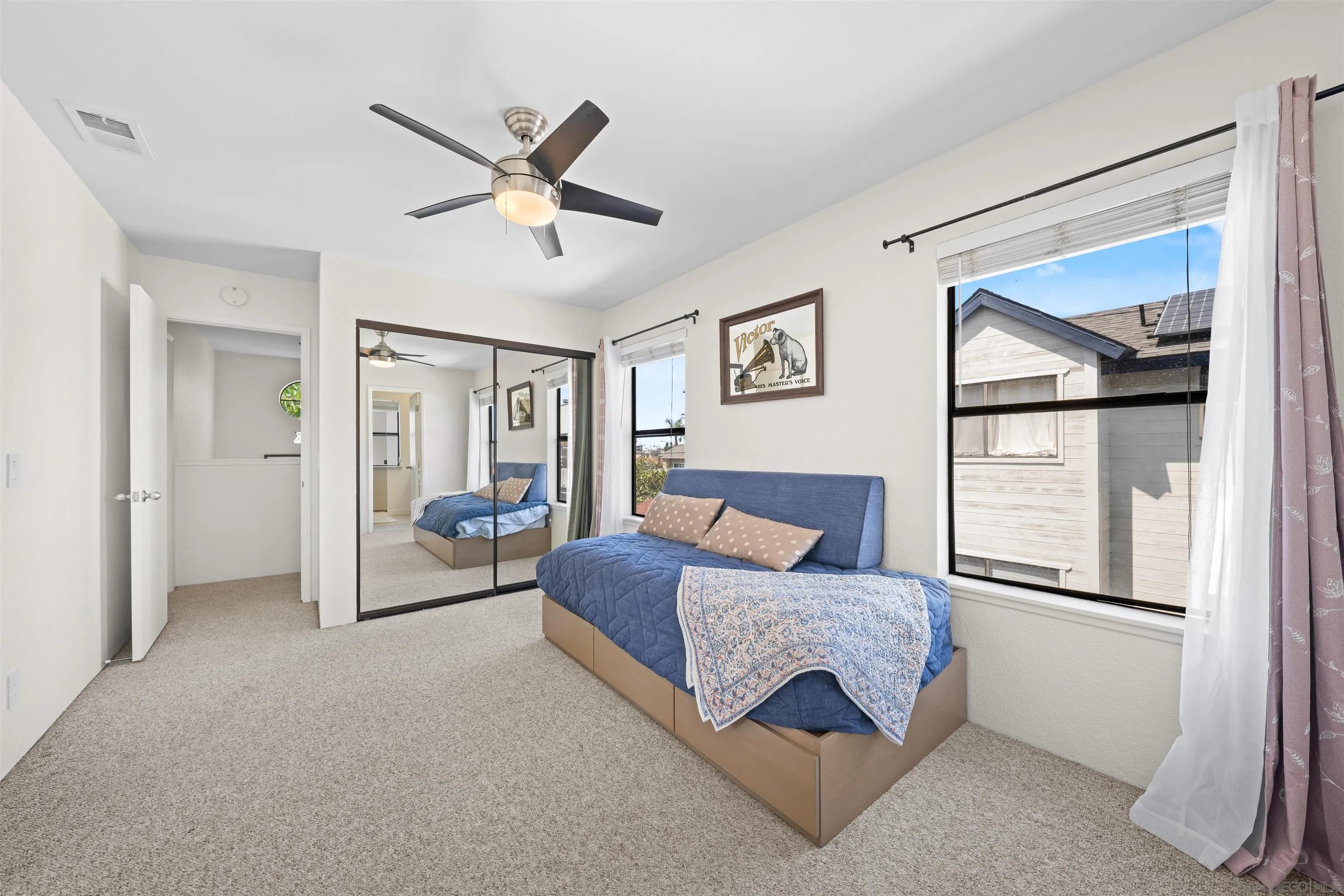 Furnished bedroom with a blue-covered bed, mirrored closet doors, and a large window.