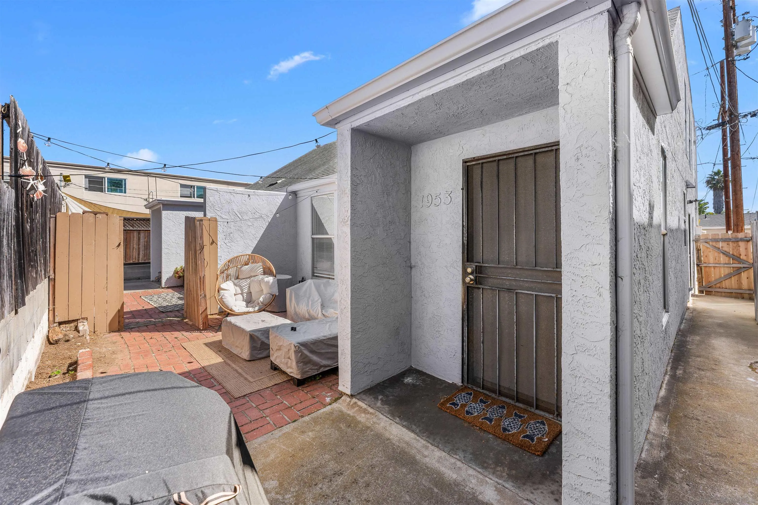 White stucco home entrance marked 1953 beside a brick patio with outdoor seating.