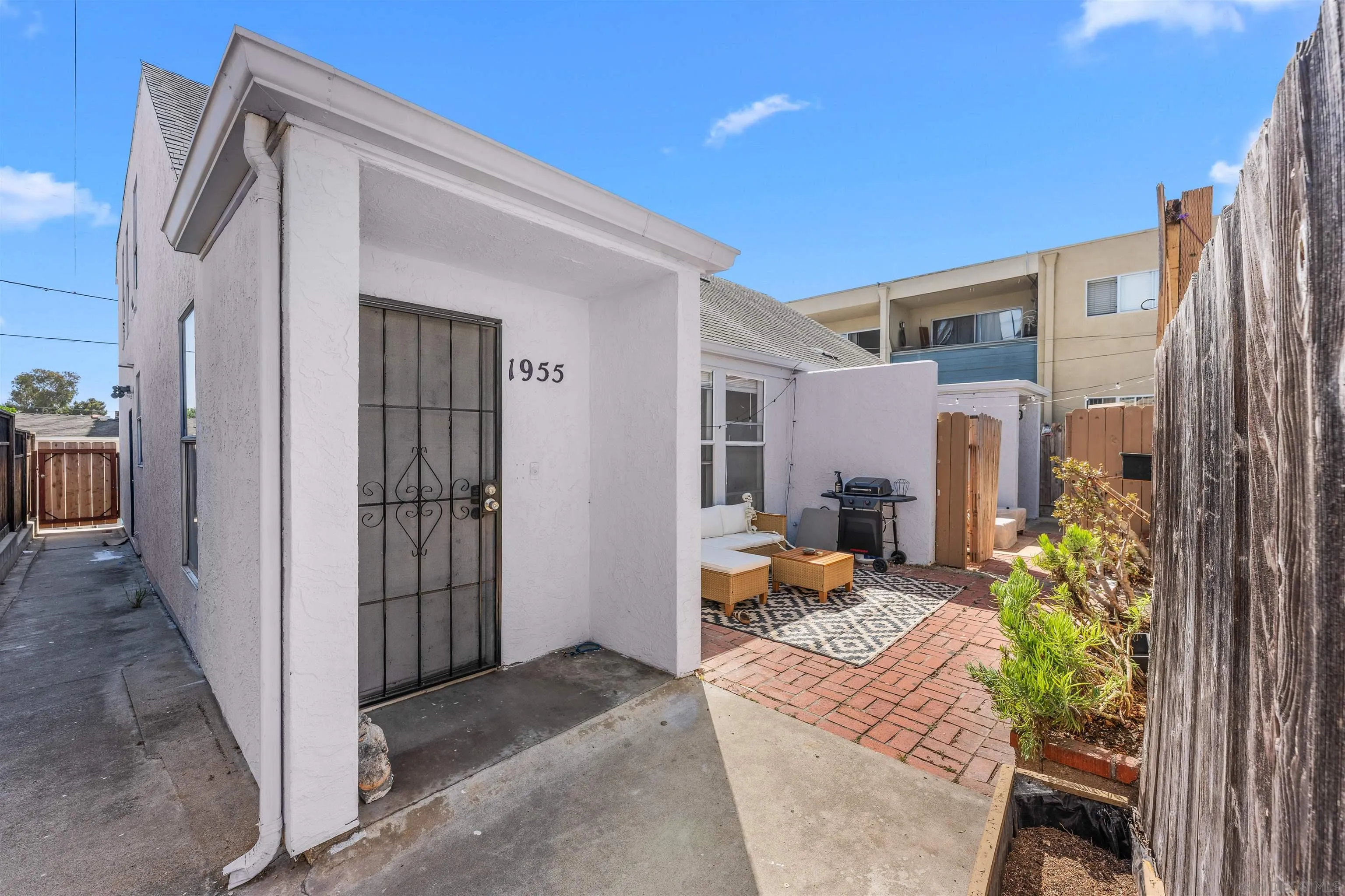 White stucco home entrance with a black security door opening onto a brick patio with outdoor seating.