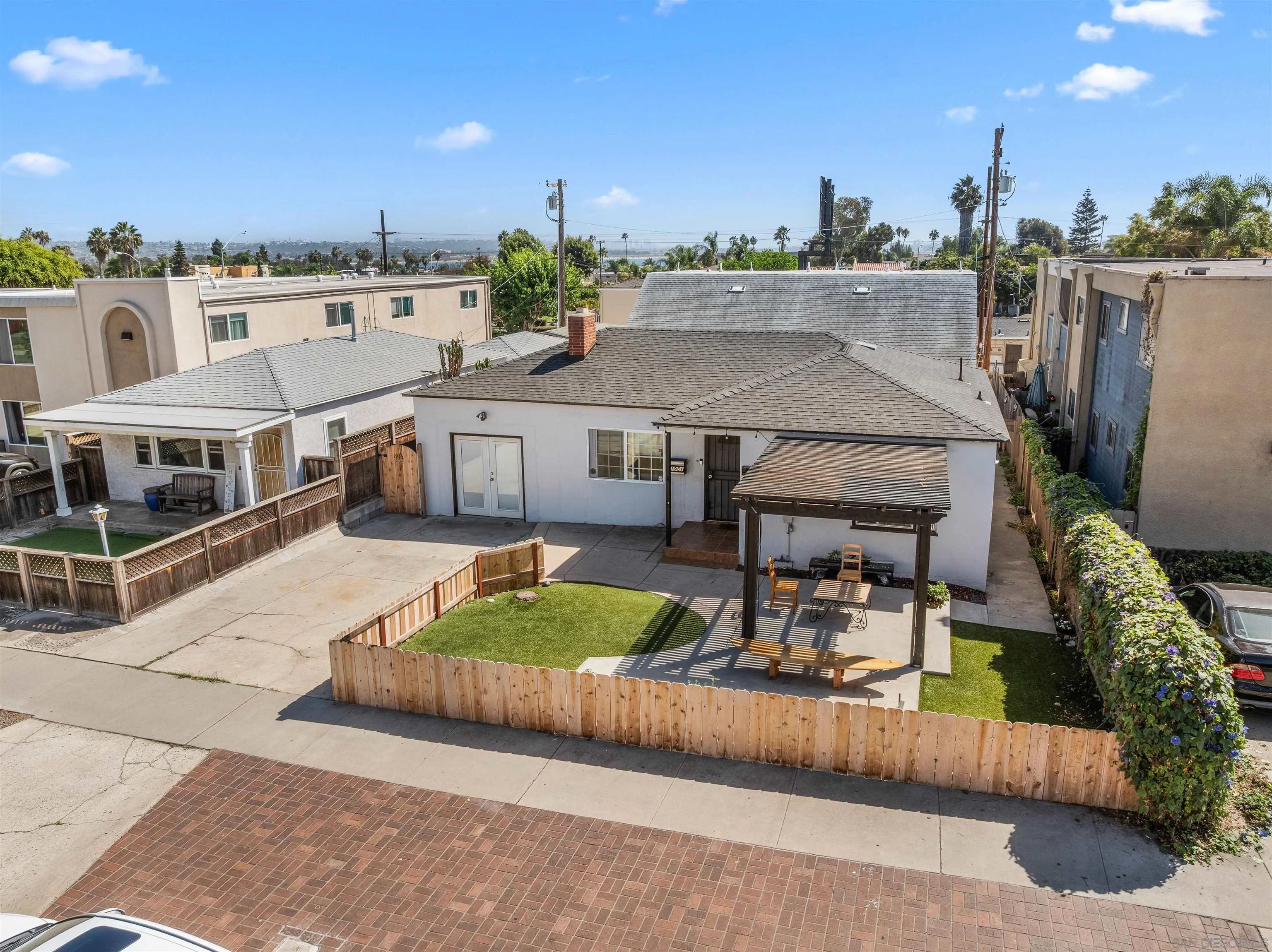 Rear exterior of a white home with a fenced lawn, patio, and pergola.