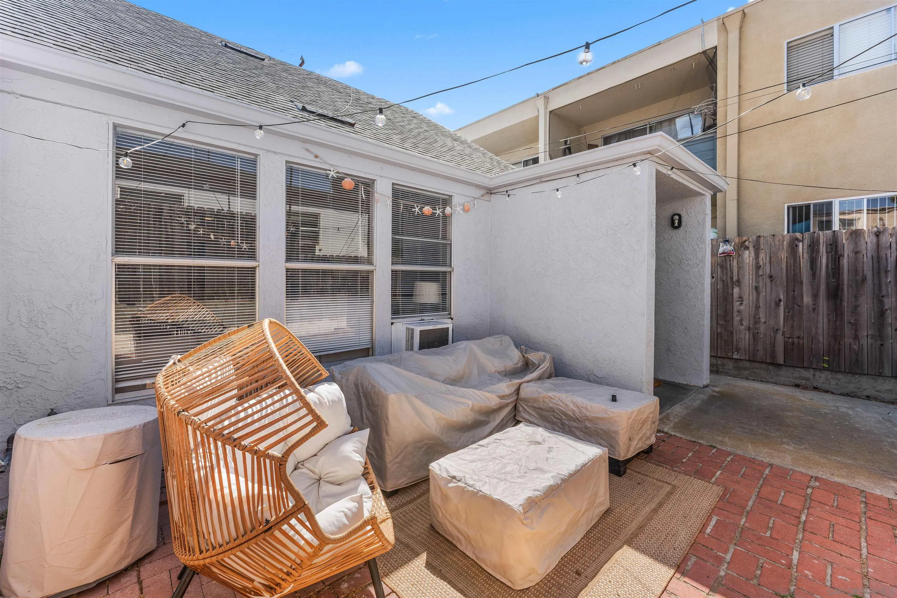 Furnished patio with wicker seating, covered lounge furniture, brick paving, and string lights.