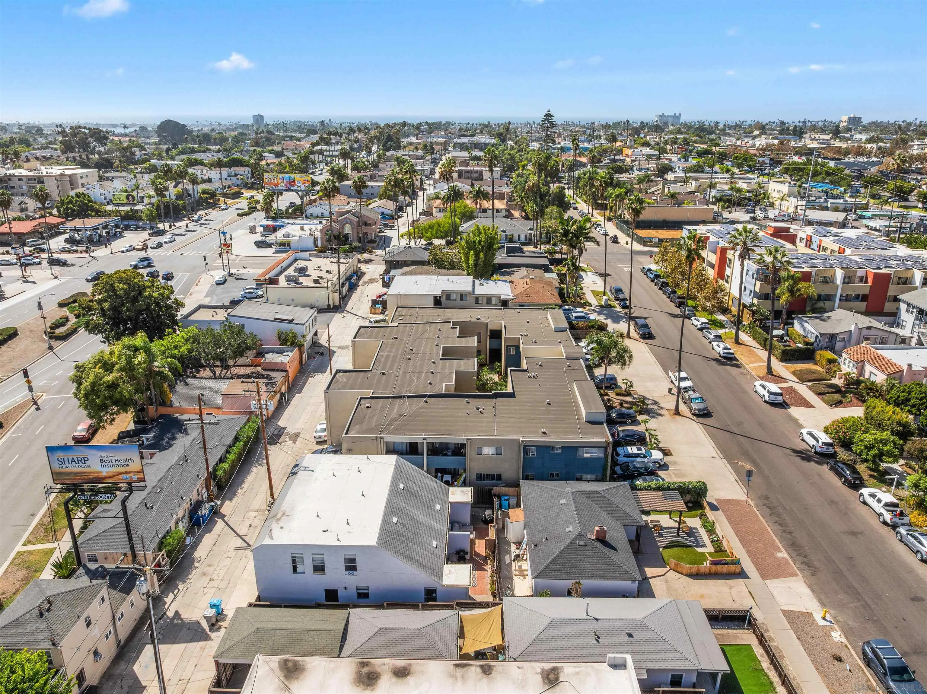 Aerial view of a flat-roofed multifamily property amid palm-lined streets and dense San Diego neighborhoods.