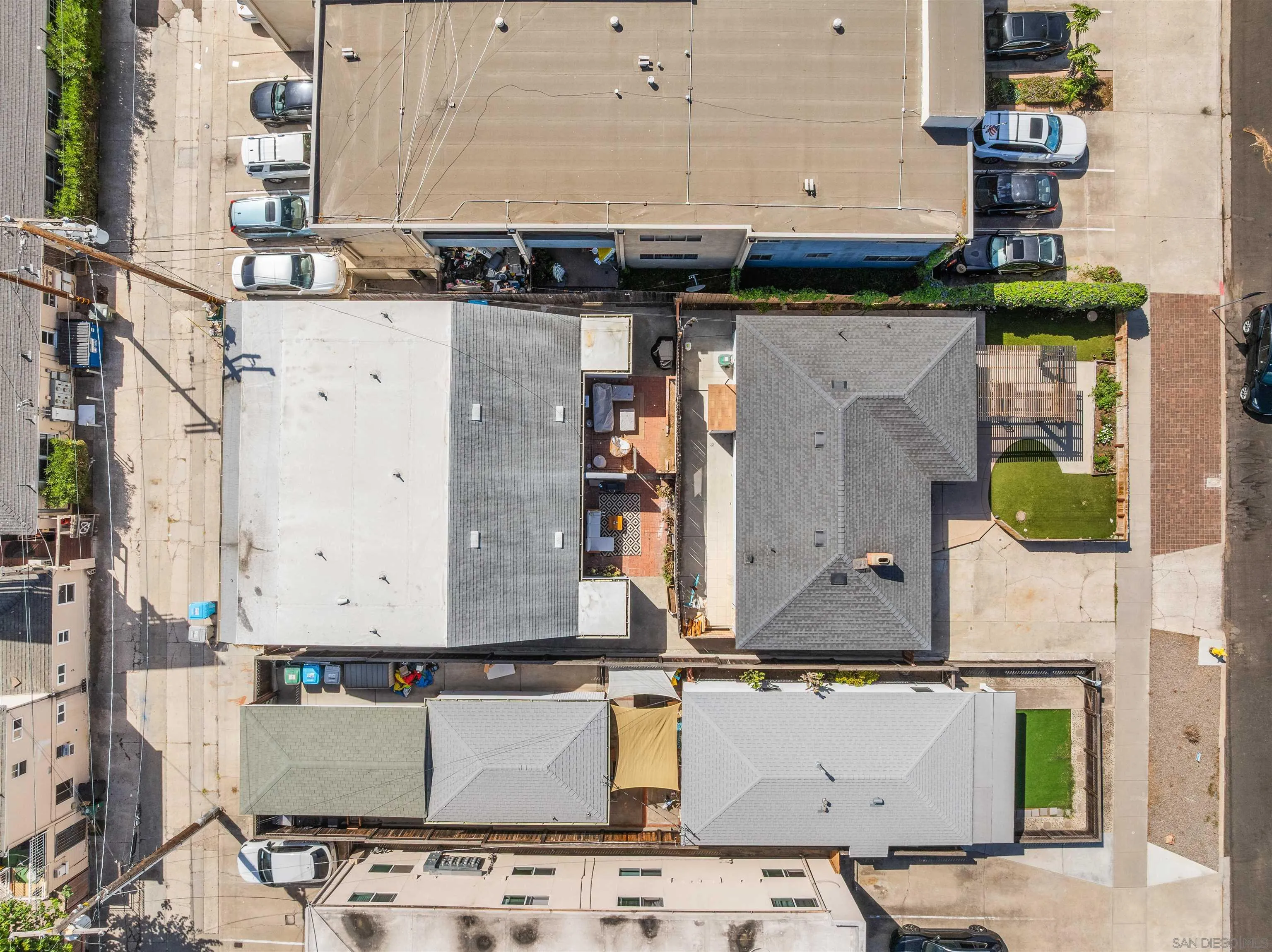 Aerial view of neighboring homes, rooftops, parking areas, and landscaped yards.