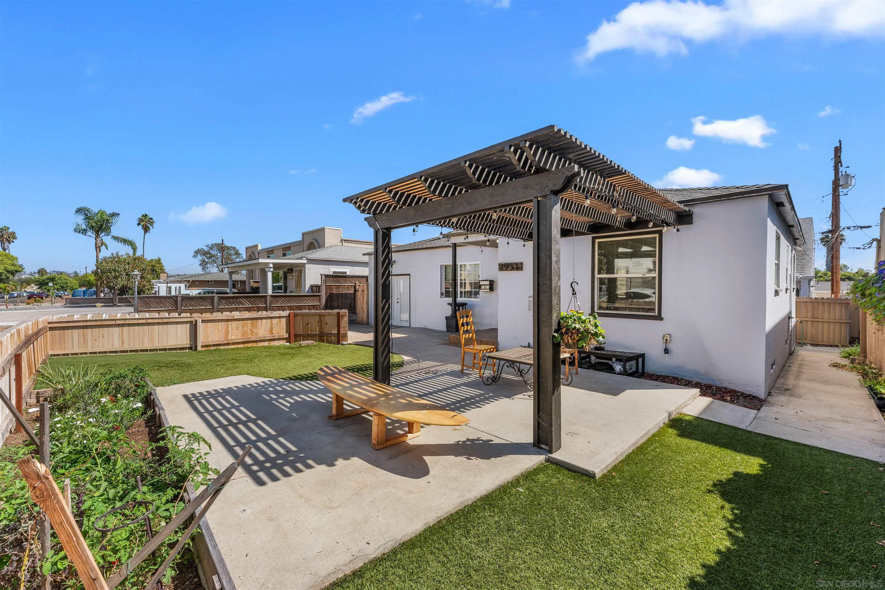Backyard patio with a dark timber pergola, outdoor seating, lawn, and raised garden beds.