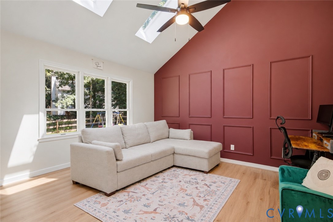 Living room with a gray sectional, burgundy paneled wall, skylights, and ceiling fan.