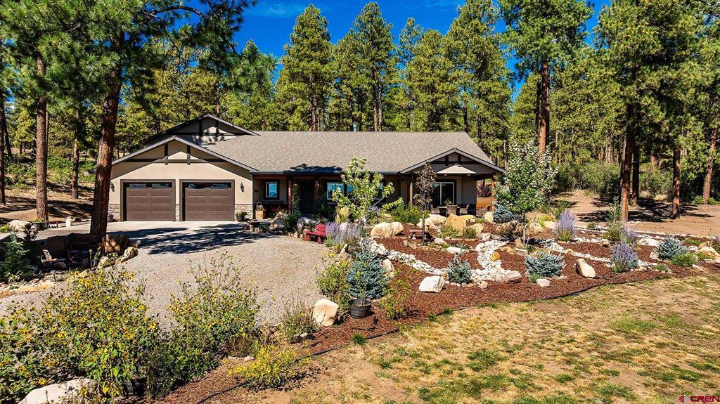 Single-story home with a two-car garage, landscaped yard, and pine trees.