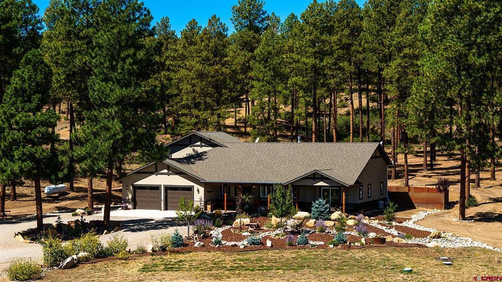 Single-story home with a two-car garage and landscaped rock beds among pine trees.