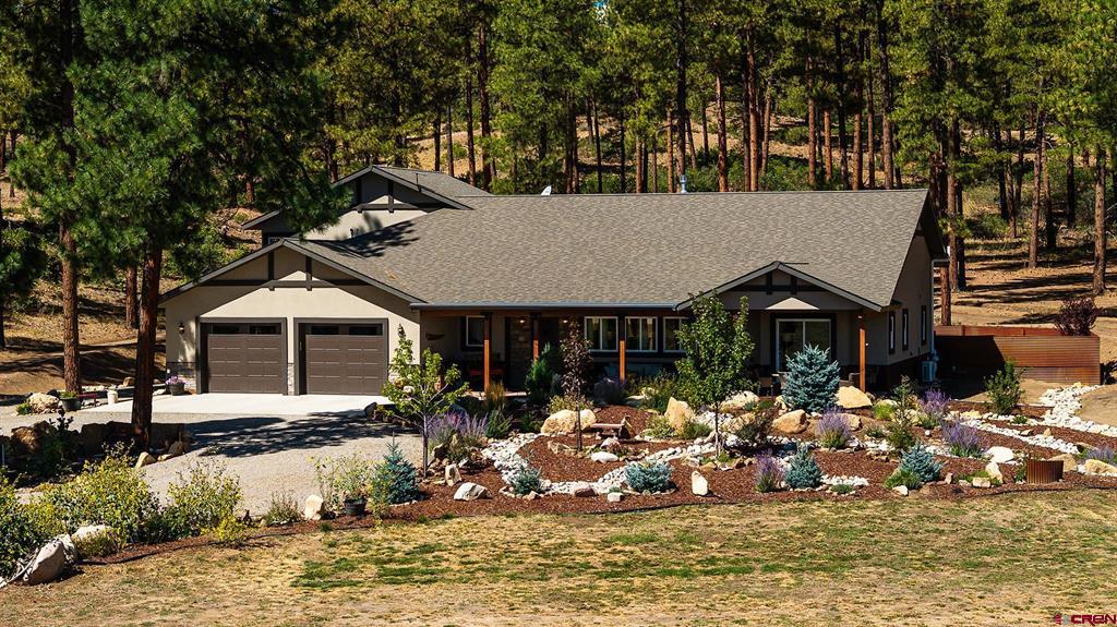 Single-story home with a two-car garage and rock landscaping among pine trees.