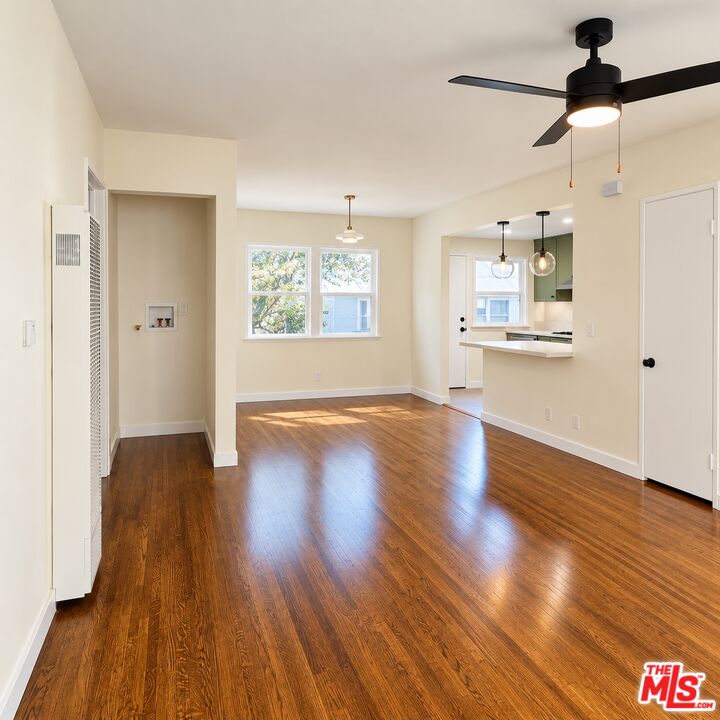 Vacant living and dining area with polished wood floors, a black ceiling fan, and a kitchen pass-through.