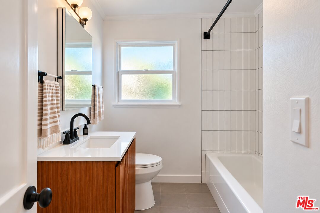 Renovated bathroom with a wood vanity, frosted window, and white-tiled bathtub surround.