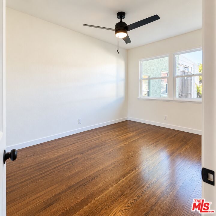 Vacant room with hardwood floors, a black ceiling fan, and a wide window.
