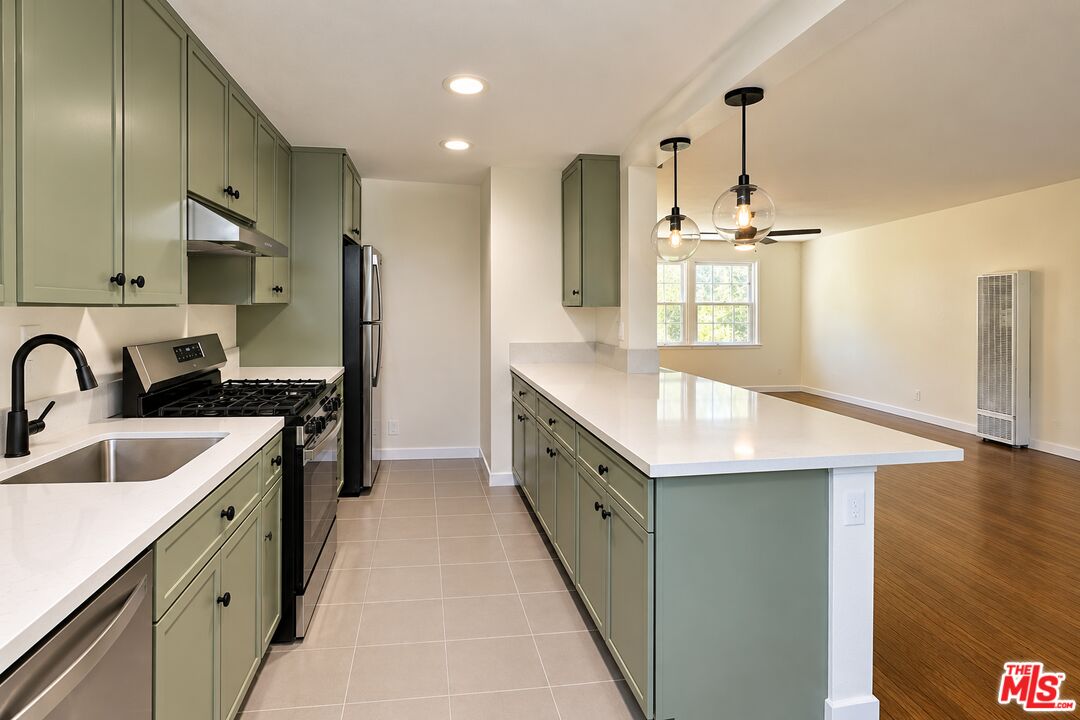 Open-plan kitchen with sage-green cabinets, a large white island, and stainless steel appliances.