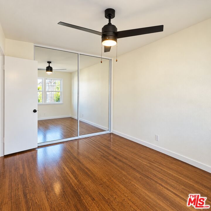 Empty bedroom with wood flooring, mirrored closet doors, and a black ceiling fan.