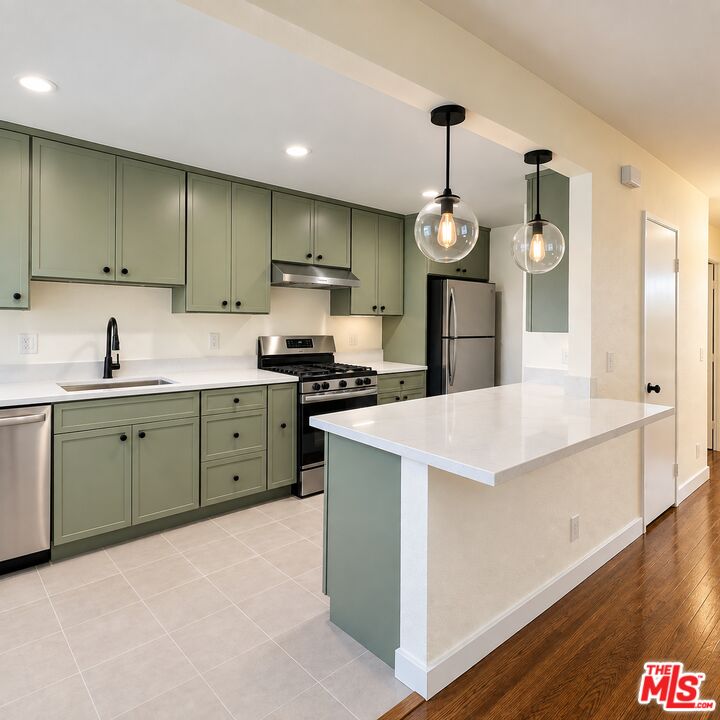 Kitchen with sage-green cabinets, stainless steel appliances, and a large white peninsula.