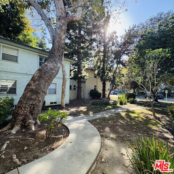 Two-story residential building beside a curved walkway shaded by mature trees.
