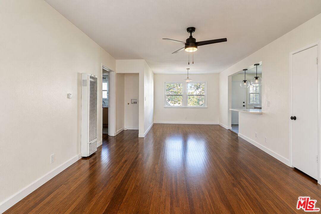 Vacant living and dining area with dark hardwood floors, a ceiling fan, and a kitchen pass-through.