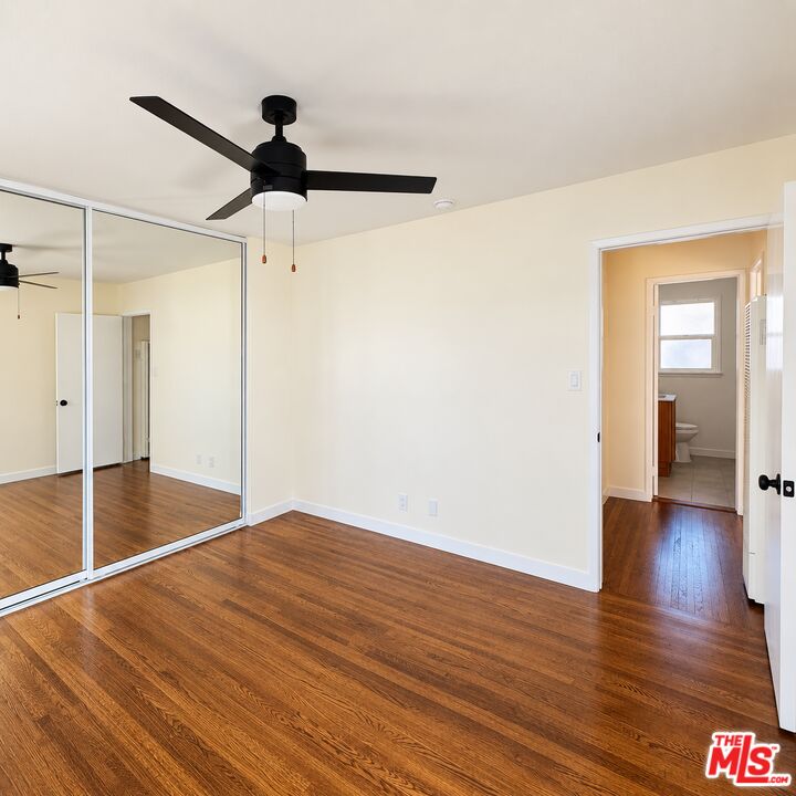 Vacant bedroom with mirrored closet doors, hardwood floors, and a black ceiling fan.