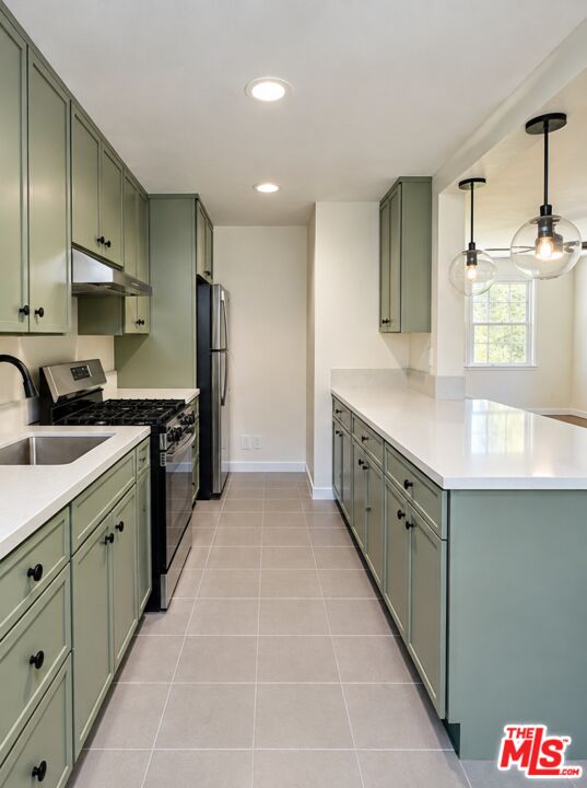 Galley kitchen with sage-green cabinets, white island countertop, stainless steel appliances, and pendant lights.